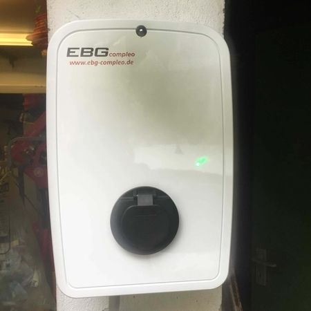 Eine an der Wand montierte Ladestation für Elektrofahrzeuge mit einer grünen Kontrollleuchte.
