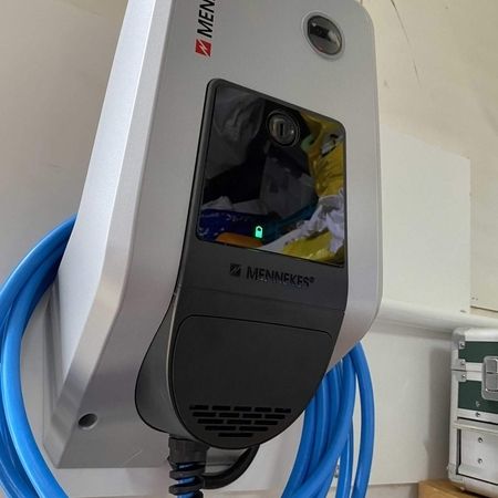Ein MENNEKES-Ladegerät für Elektroautos mit blauem Spiralkabel, das an einer Wand montiert ist.