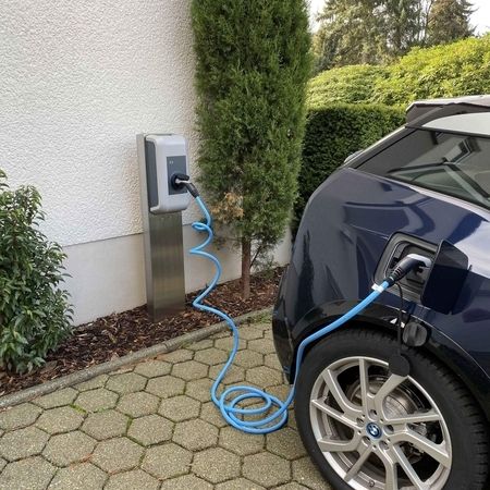 Ein Elektroauto, das an einer Ladestation neben einem Haus angeschlossen ist.