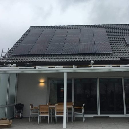Haus mit Sonnenkollektoren auf dem Dach und einem Innenhof mit Möbeln.