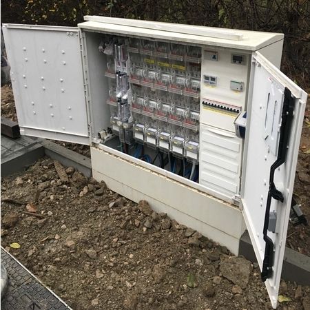 Offener Schaltschrank im Freien mit Verkabelung und Schaltern auf schmutzigem Boden.