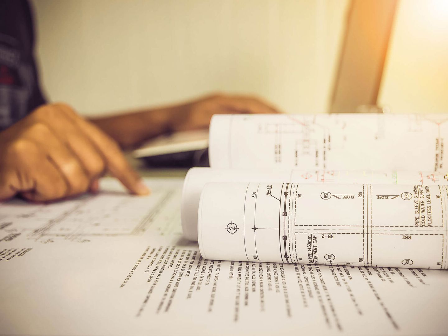 Person, die Architekturpläne auf einem Schreibtisch überprüft, warme Beleuchtung.